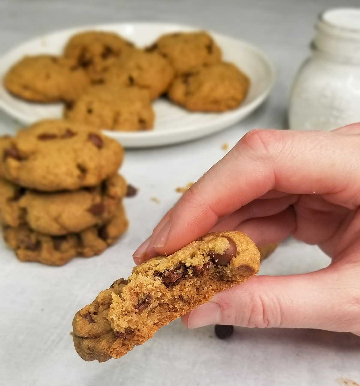 holding cookie up to camera with plate of cookies and cup of milk in background