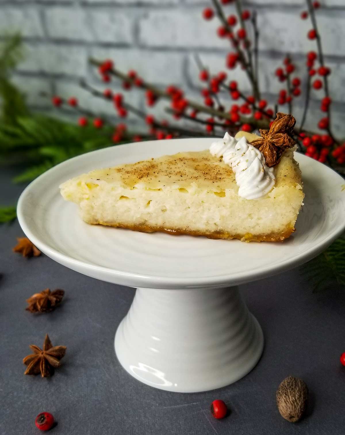 picture of 1 piece of eggnog cheesecake on cake stand with christmas garnishes in background