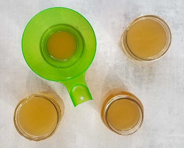 overhead picture of bone broth in mason jars with funnel