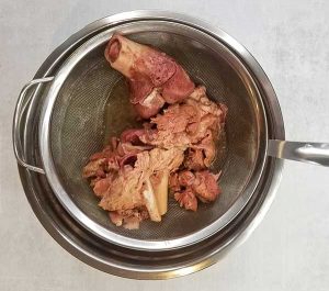 bones in strainer on top of large bowl with bone broth