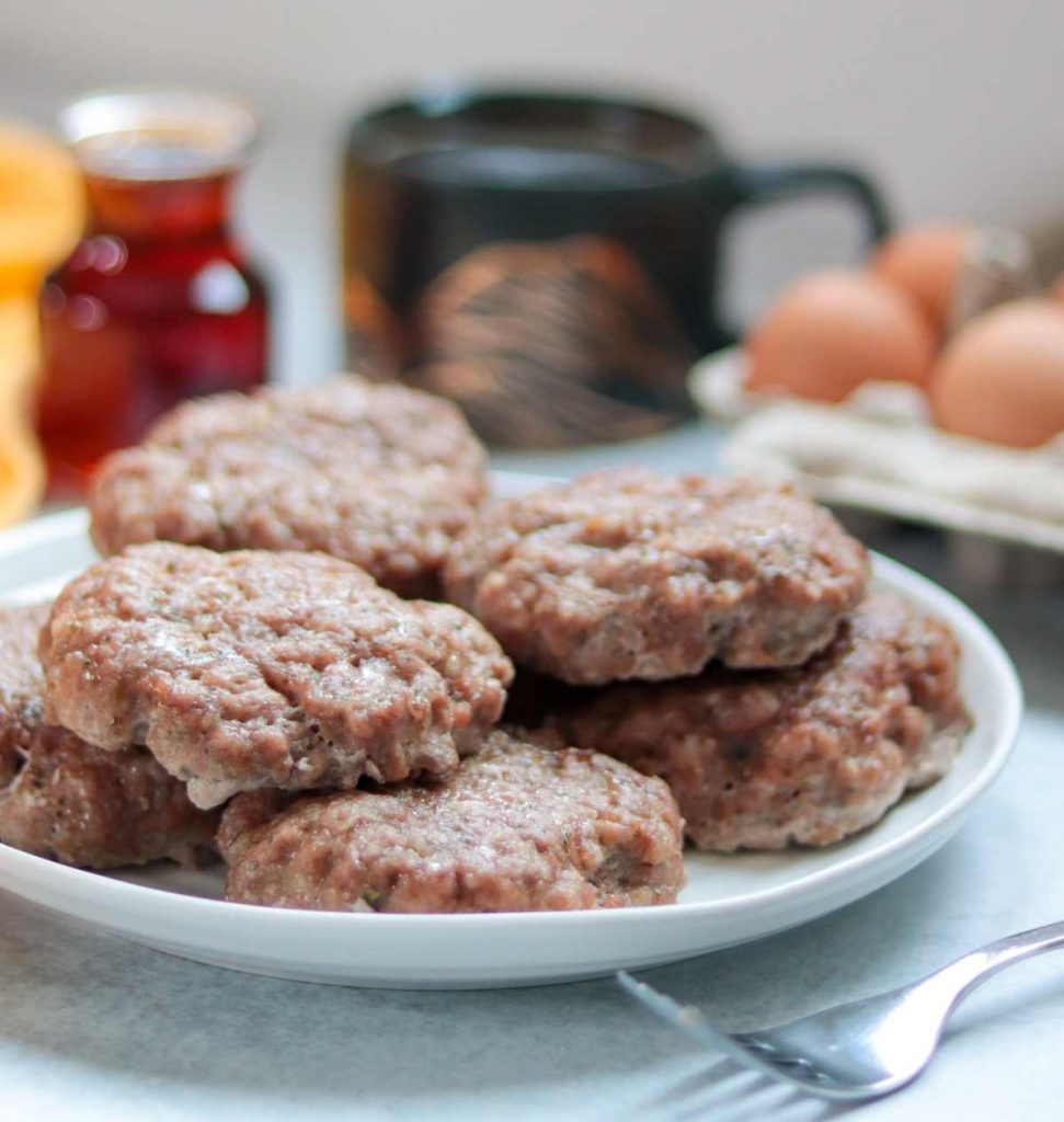 Maple breakfast sausage recipe (oven baked) on white plate with cup of coffee