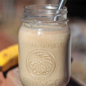 Peanut butter banana oat smoothie in glass jar with straw