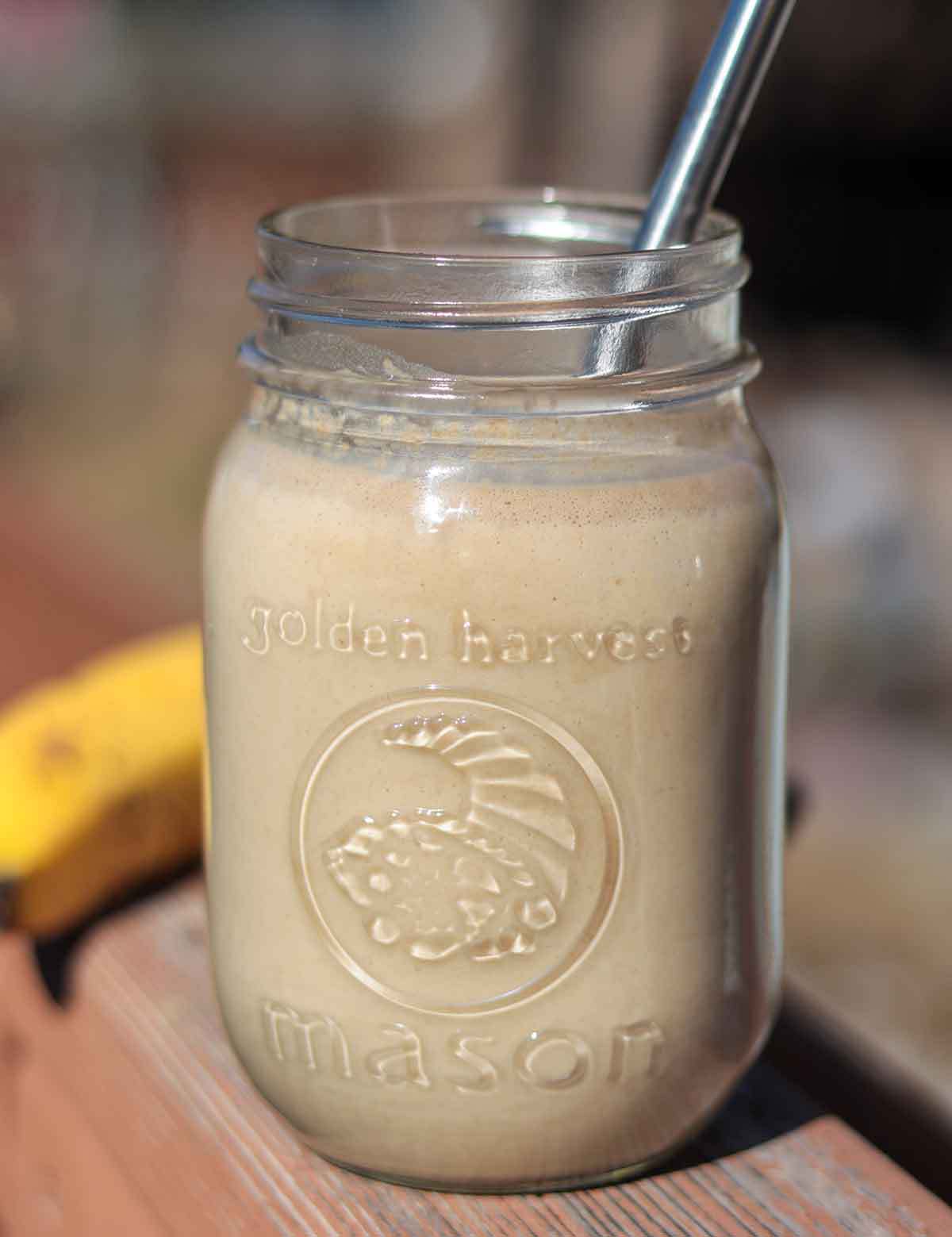 Peanut butter banana oat smoothie in glass jar with straw