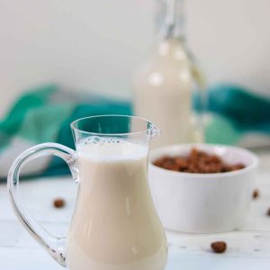 Pitcher of tiger nut milk with bowl of tiger nuts and bottle of milk behind it