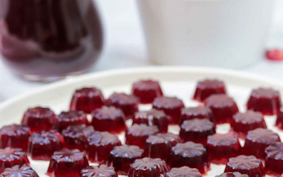 Pomegranate gelatin gummies on plate with bowl of pomegranate in back