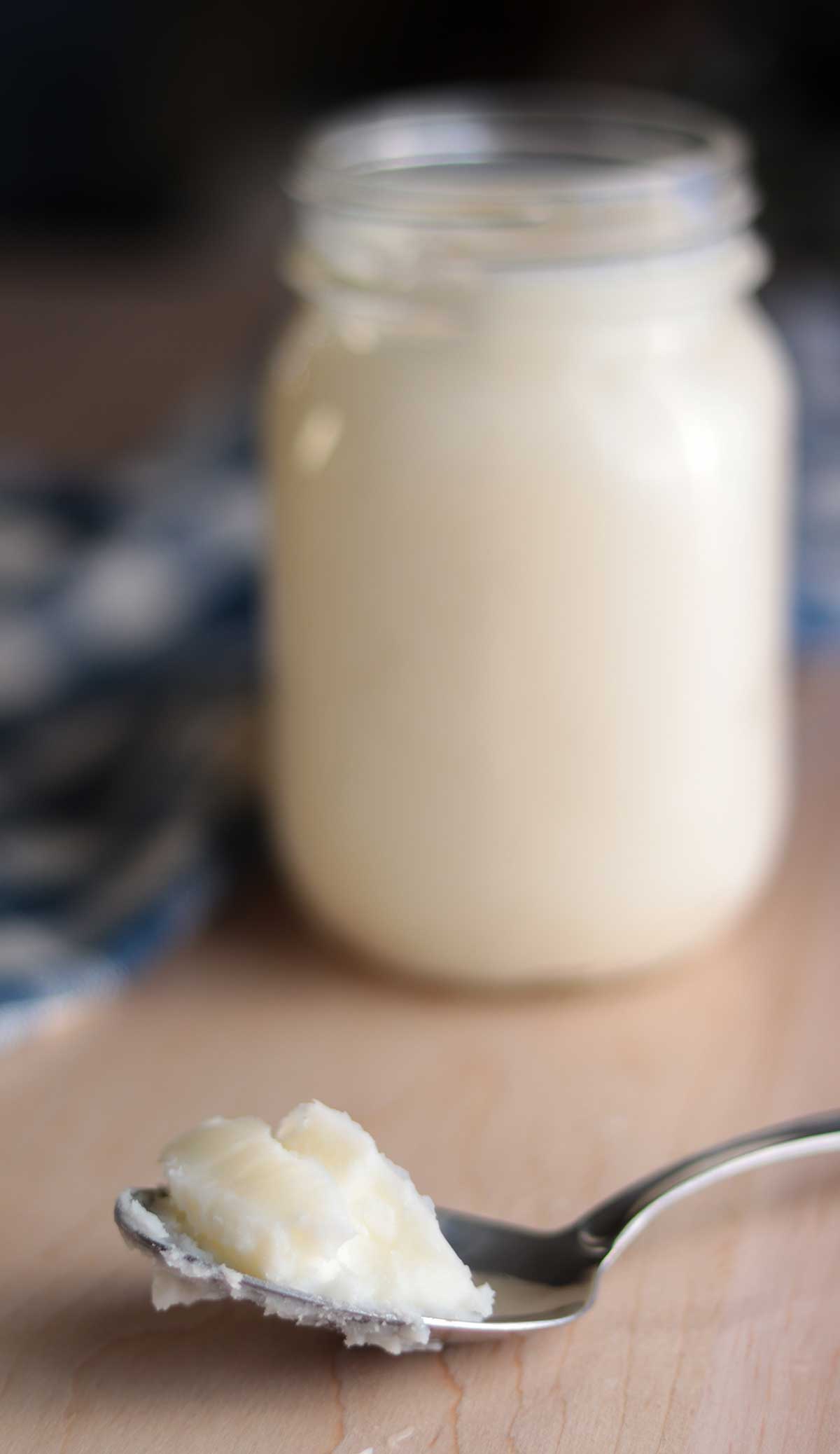 A spoonful of beef tallow in front of a mason jar filled with cream colored beef tallow
