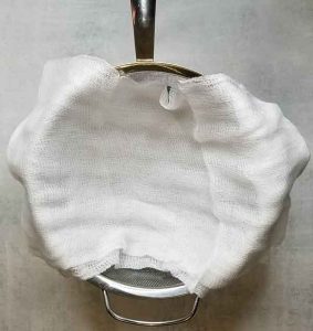 Cheesecloth draped overtop of a large metal strainer