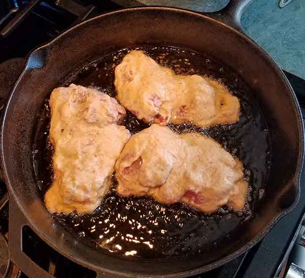 three pieces of fried chicken frying in cast iron pan