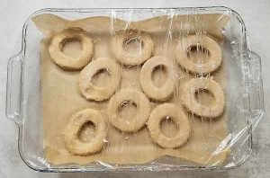 Cut out doughnuts in glass dish on parchment paper covered with oiled plastic wrap to rise for 1 hour.