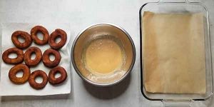 Cooked doughnuts lined up beside maple glaze and glass dish lined with parchment paper