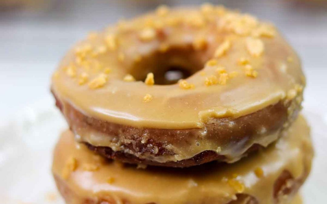 Stack of three glazed donuts with rest of donuts on cooling tray in background