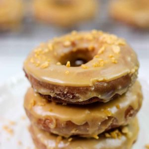 Stack of three glazed donuts with rest of donuts on cooling tray in background