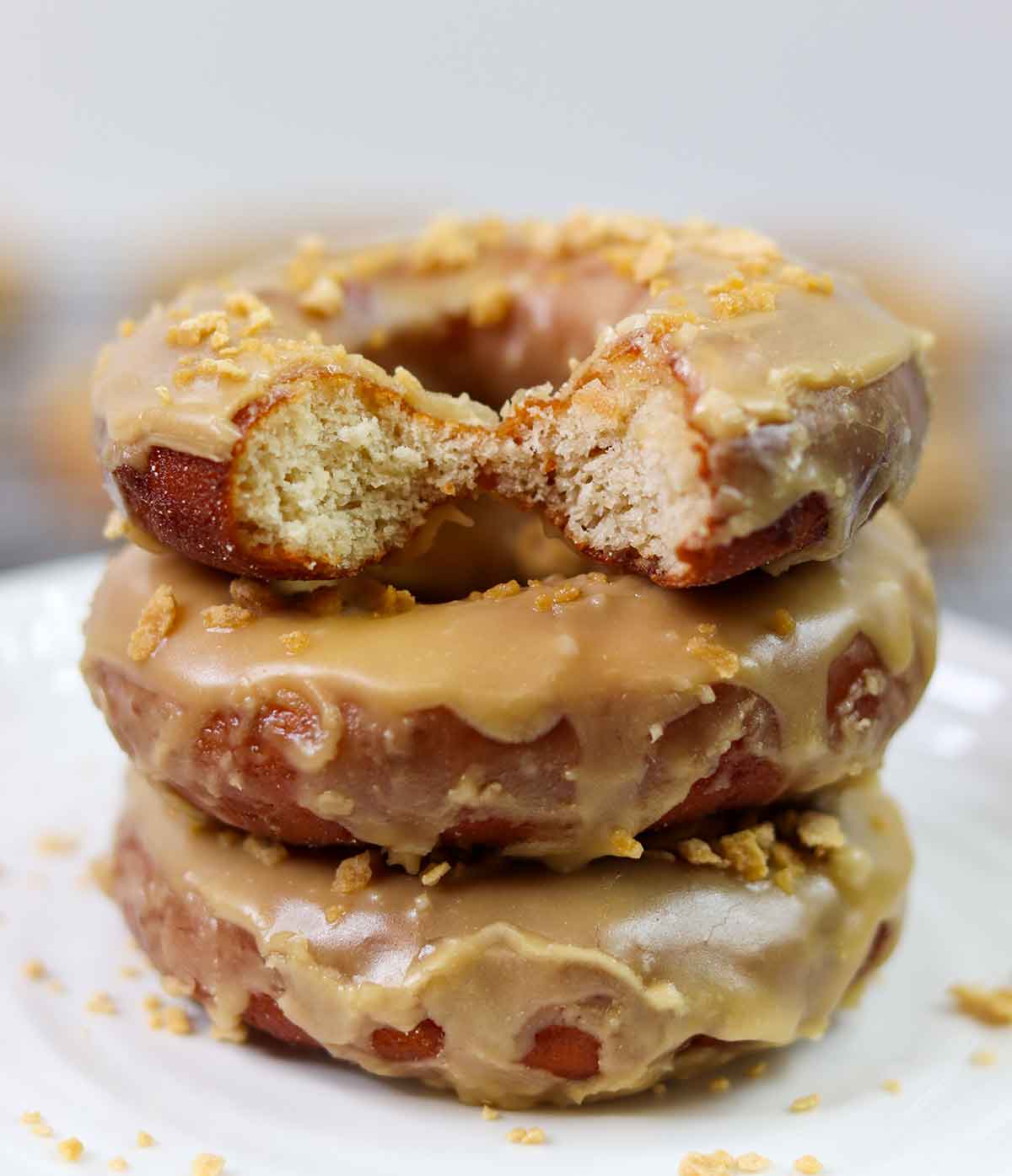 Three glazed donuts stacked up with a bite taken out of the top one