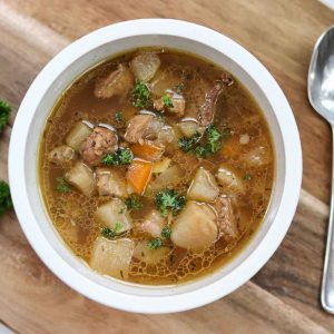 Bowl of stew on a cutting board with fresh parsley and a spoon