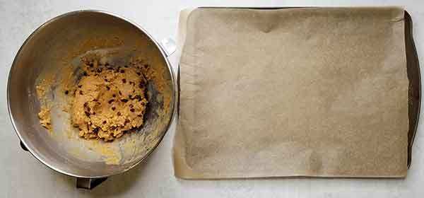 mixed dough in metal bowl sitting beside baking sheet with parchment