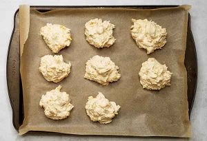 Biscuit dough formed into round circles on baking sheet with parchment paper