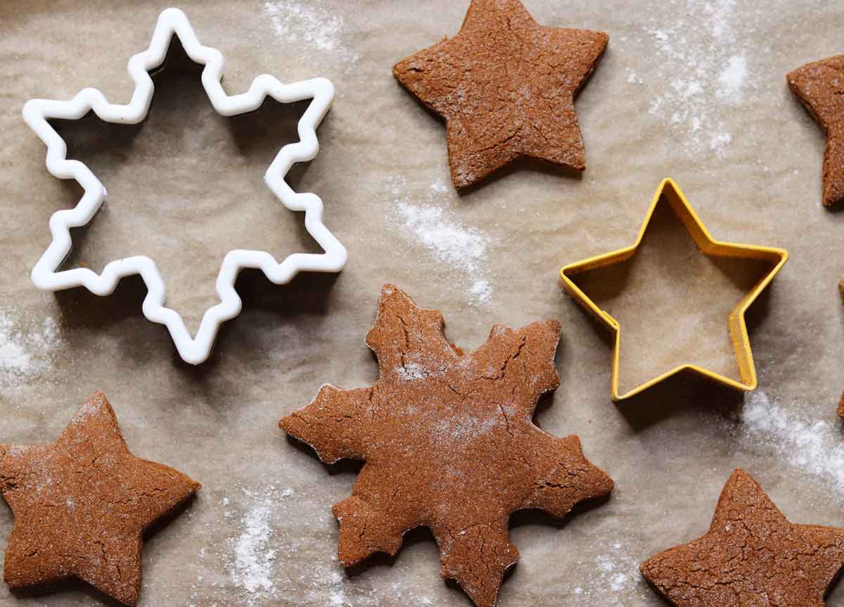 Cassava ginger bread cookies on parchment paper sitting beside cookie cutters