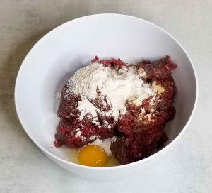 Wet and dry ingredients added to raw ground caribou in bowl