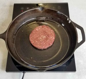 Raw caribou burger in cast iron pan