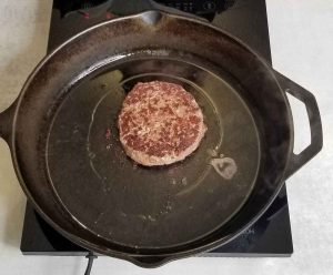 Bear burger in cast iron pan with one side browned