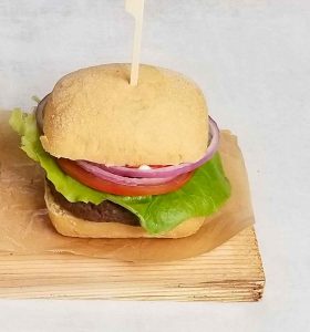 Assembled caribou burger placed on wooden plank with brown parchment paper