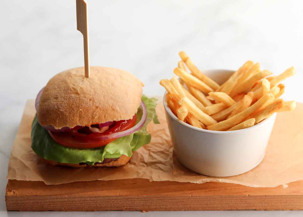 Overhead side view of caribou burger with a side fries placed on a wooden plank