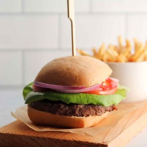 Caribou burger placed on a wooden cutting board with a side of fries in the background