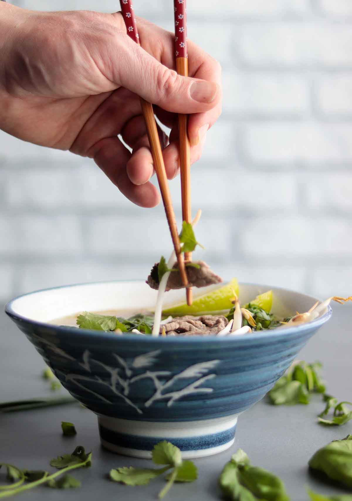 Keto pho being eaten with chop sticks out of a blue ceramic bowl