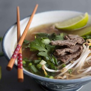 Keto Pho in blue ceramic bowl with chopsticks crossed and balanced on the sideKeto pho soup recipe (easy & fast) This keto pho soup recipe is fast and easy to make because it uses store-bought pho broth and pre-spiralized kohlrabi noodles. Below I also provide options for making your own broth, as well as other low carb noodle alternatives. Recipes substitutions and variations (H2) Store-bought pho broth substitutions: To make this recipe super quick and easy, I made use of premade pho broth from the store. However, if you want to keep the ingredients super clean you can also use your own homemade bone broth and then add pho seasonings to it. This could include star anise, cloves, cinnamon, cardamom, and coriander. You can also add lime, onion, ginger, salt and fish sauce. Beef rouladen substitutions: Traditional pho recipes are generally made with thinly sliced beef. To make things easier, I bought pre sliced beef rouladen. This is essentially long, thin strips of beef that are super easy to slice up into smaller pieces. You can also use any other cut of beef and slice it up as thinly as possible using a meat slicer or sharp knife. I have also made this soup with thinly sliced “hot pot” pork shoulder or chicken and it’s also fantastic. I found these in the frozen meat section of the grocery store. Kohlrabi noodle substitutions: For this recipe, I highly recommend using Mann's Kohlrabi “Linguine” which I get at my local Save-On-Foods. If you aren’t able to access this, you can also spiralize your own kohlrabi noodles with a vegetable spiralizer. Or you can find other spiralized vegetables to use instead as your noodle base such as sweet potatoes, zucchini, or butternut squash. Or if you are not concerned about making this lower in carbohydrates, you can of course use regular rice noodles. Shallot substitutions: Instead of using shallots, you can also swap it out for regular white onion. Or even dehydrated onion flakes. Fresh herb substitutions: Instead of using fresh basil and cilantro, you can swap it out for dried basil and cilantro. If you do this though, add them to your pot at the same time you add your noodles, instead of at the end. This will help infuse the broth with the herbs flavour. Just keep in mind you will not get the fresh, intense flavour of the fresh herbs if you do this. The fresh herbs also provide a really beautiful presentation to your dish. Green onion substitutions: Instead of green onions, you can also swap it out for fresh chives. If you aren't able to get fresh, you can use dehydrated chives. If you do this, add your chives at the same time you add your noodles. This will allow the dehydrated chives to rehydrate and infuse their flavour into the broth. Lime substitutions: The lime is used for garnish and flavour at the end. If you don't have fresh lime, you can also use store-bought lime juice. Dietary modifications for this recipe (H2) Make this recipe low FODMAP: Omit the shallot and make sure your broth does not contain garlic or onion, or any other high FODMAP vegetable. Make this recipe AIP: Avoid store-bought broth. Use your own bone broth and then add in AIP friendly ingredients such as ginger, fish sauce, garlic, onion, and cinnamon. Make this recipe candida diet friendly: Avoid broth that contains sugar or yeast. Or alternatively, make your own broth using bone broth and add seasonings such as star anise, cloves, cinnamon, cardamom, coriander, lime, ginger and salt. Make this recipe even lower carb: Store-bought pho broth isn't super high in carbohydrates, although the stuff I used does add about 5 g of carbohydrates per serving of this soup. To make this recipe even lower in carbs, use your own homemade pho broth. Pro tips for this recipe: (H2) Add your fresh herbs, bean sprouts and green onions at the end Adding your herbs and garnishes at the end will make for a beautiful presentation and gives the soup a fresher, crunchier texture. Don’t cook the meat for too long In this recipe, I call for adding the meat at the very end. Because the meat is so thinly sliced, you don’t want to overcook it and have it be chewy and not as tender. The meat cooks really fast so it only needs a few minutes to cook through. Frequently asked questions: (H2) How long does this soup last in the fridge? This soup will last in the fridge for up to 1 week but I recommend eating it up within a few days for ultimate freshness. This soup freezes very well, so if you aren’t able to finish it up, portion it out and freeze it in glass containers. Does this low carb pho freeze well? This soup freezes incredibly well, even with the fresh herbs and garnishes on top. I make this soup for weekly meal prep and portion it out and freeze it. Then I take it out the night before I plan to eat it for lunch. Pin this recipe for later (H2) If you can’t make my homemade pho soup now, make sure to pin the recipe for later so you have it handy! > Tried my easy homemade pho? (H2) Please leave me a rating and review below, and post a picture of the dish to Instagram and tag me at @foodsnfeels 🙌 You might also like: (H2) If you liked my healthy pho recipe, check out my other soup recipes: Keto chicken bacon soup How to make bone broth in a crock pot Cream of mushroom soup Moose stew slow cooker Ham bone split pea soup