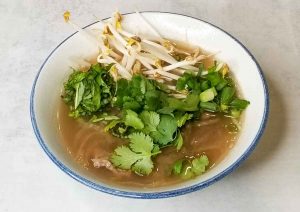 Keto pho in white bowl topped with green garnishes