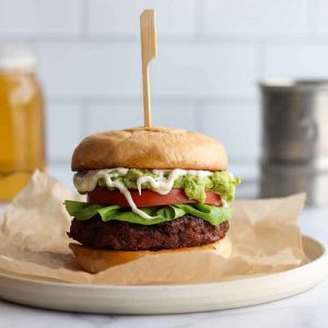 Black bear burger with all the toppings sitting placed on a round plate with lager in background