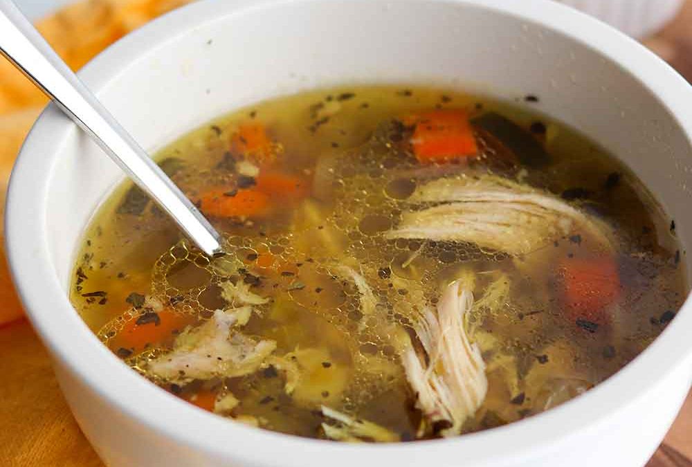 Crockpot chicken soup in a single serving white ceramic bowl with spoon