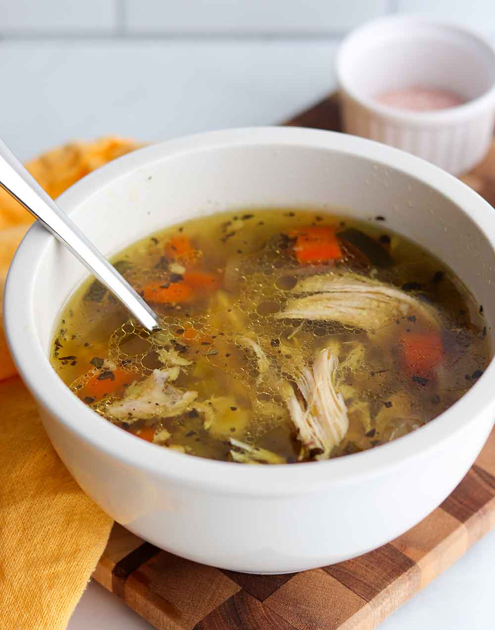 Crockpot chicken soup in a single serving white ceramic bowl with spoon