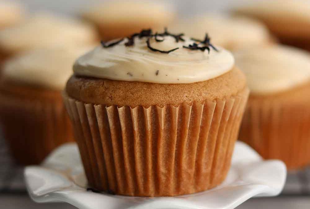 Earl grey cupcake placed on a delicate ceramic stand with batch of cupcakes sitting in background