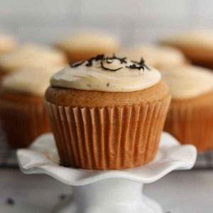 Earl grey cupcake placed on a delicate ceramic stand with batch of cupcakes sitting in background