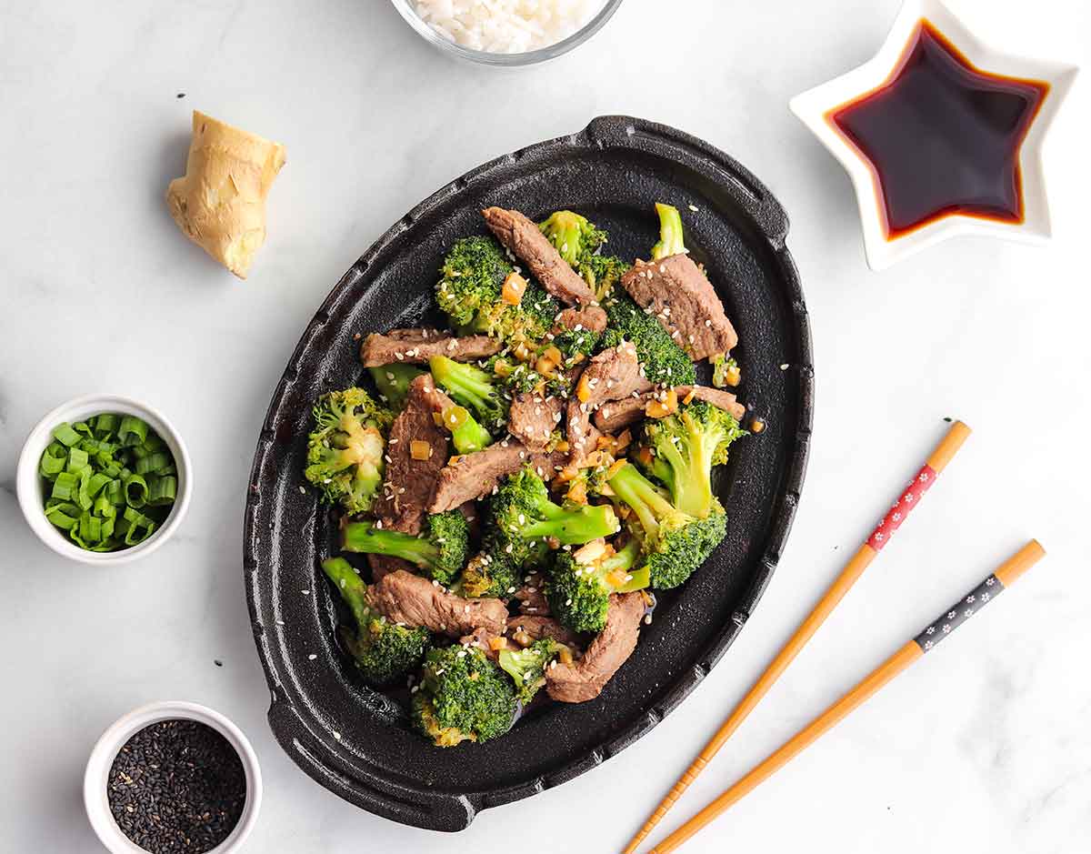 Beef and Broccoli stir fry in iron skillet surrounded by dipping sauces