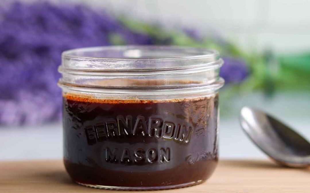 Date syrup in short mason jar placed on a wooden cutting board with a white background and a bouquet of lavender in the background