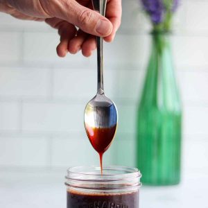 Date syrup being drizzled off a spoon into a mason jar with a beautiful bouquet of lavender in the background.