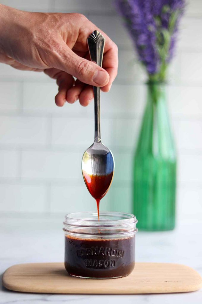 Date syrup being drizzled off a spoon into a mason jar with a beautiful bouquet of lavender in the background.
