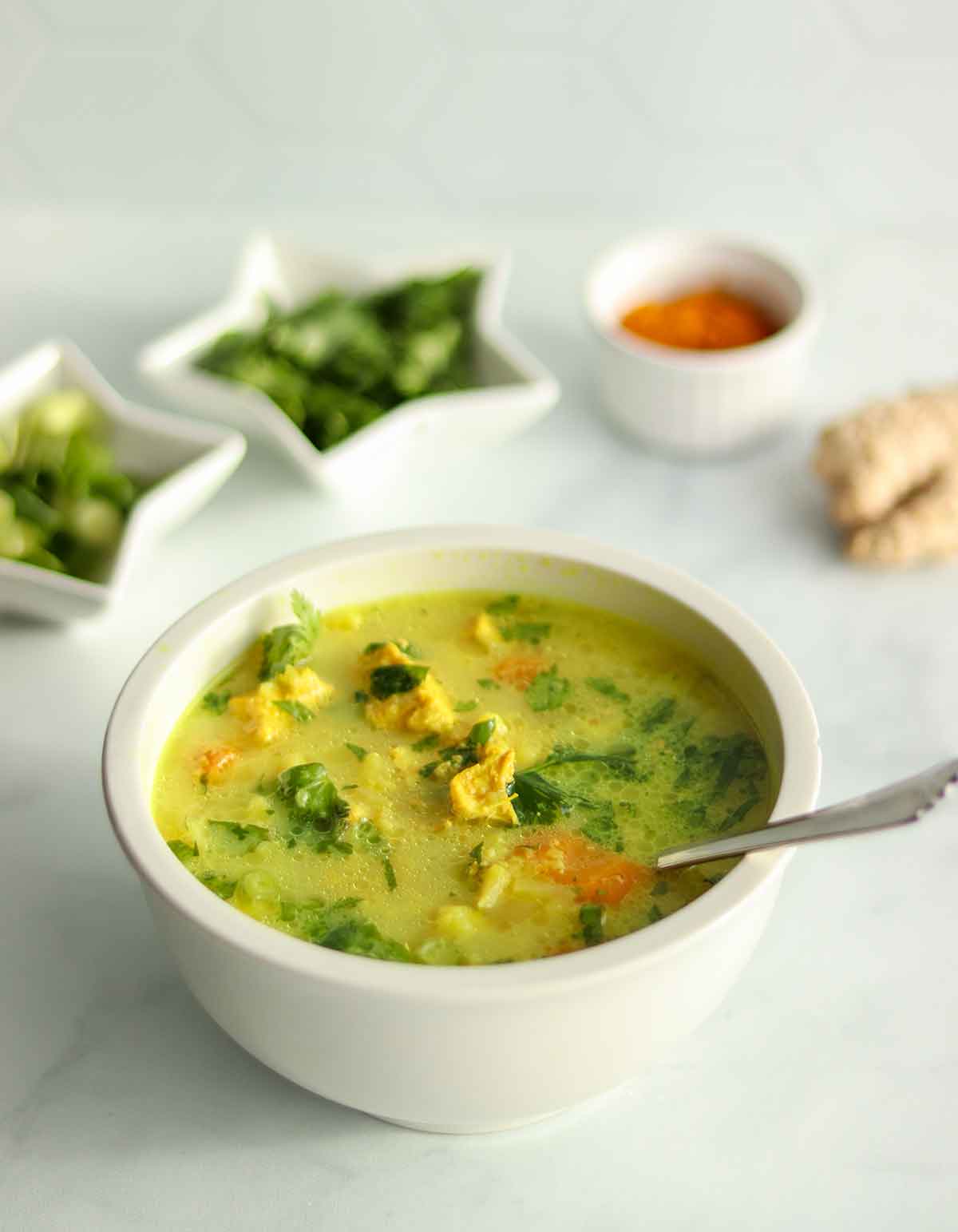 Side view of turmeric chicken soup with ingredients placed in foreground