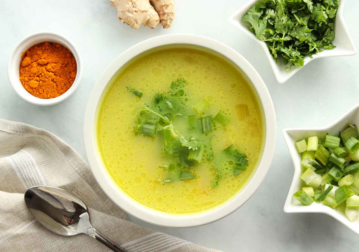 overhead view of turmeric chicken curry soup topped with a green garnish and surrounded by fresh ingredients