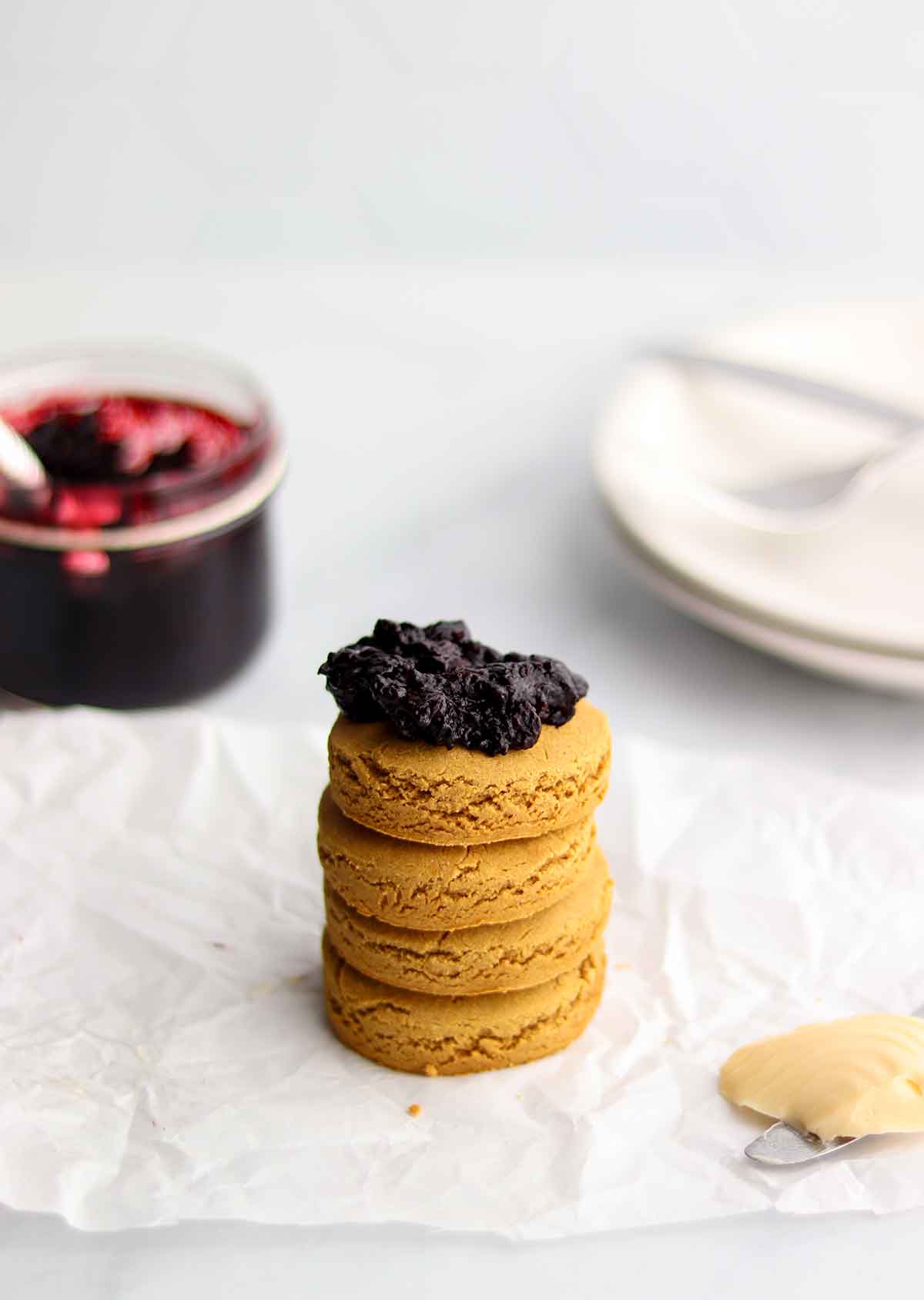 Upward view of oat flour biscuits stacked with a dollop of jam on top sitting beside a jar of jam