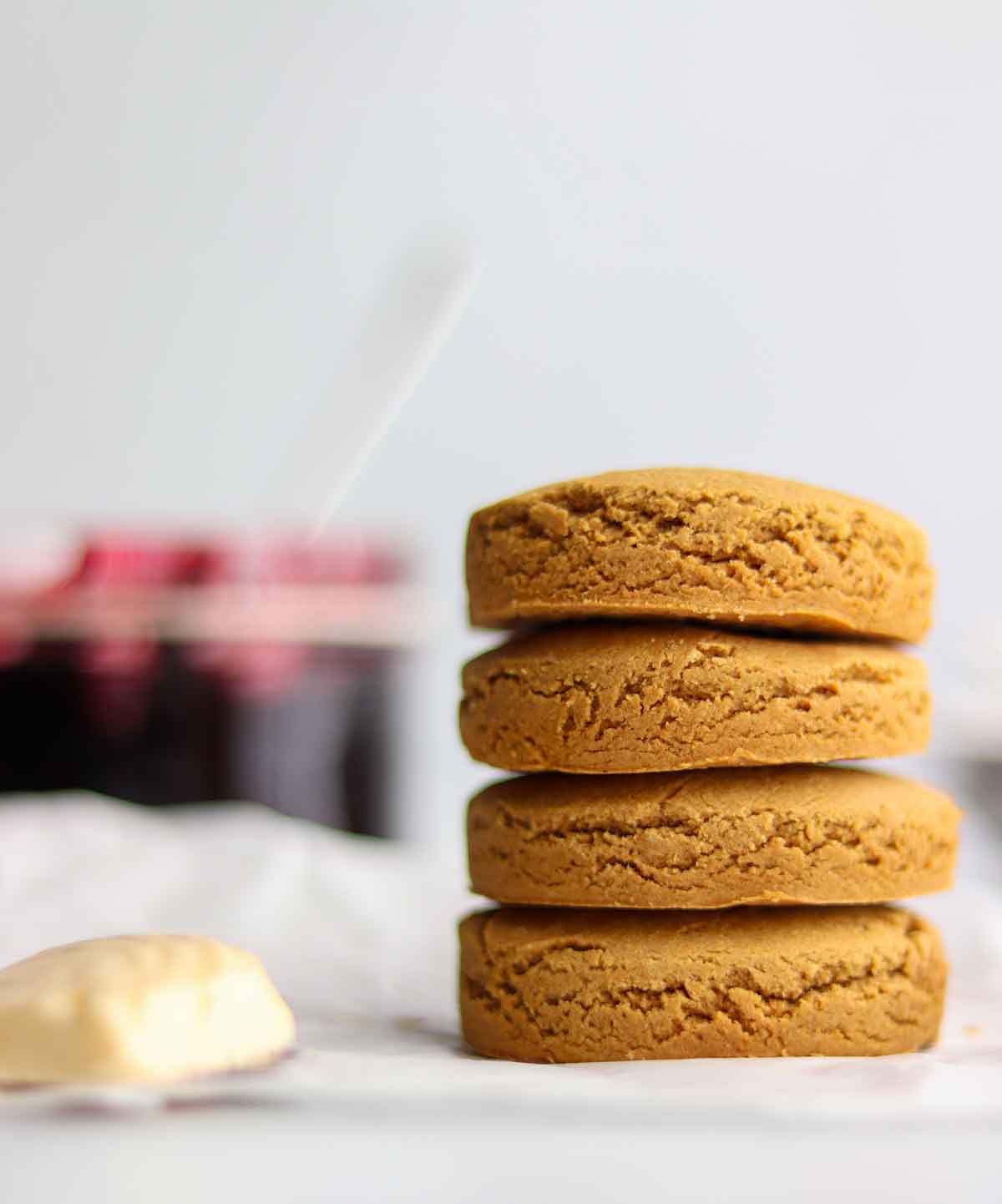 Oat flour biscuits stacked high sitting beside a cube of butter with a jar of jam placed in the background