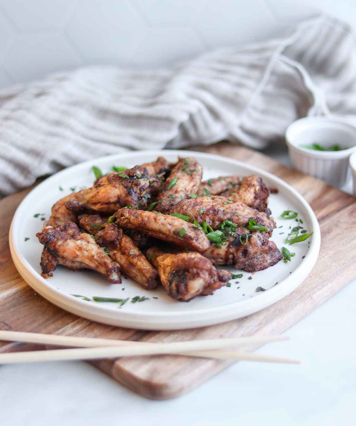 Close up side view of five spice chicken ontop of a white plate and a wooden cutting board placed beside a pair of chopsticks and sprinkled with a green garnish