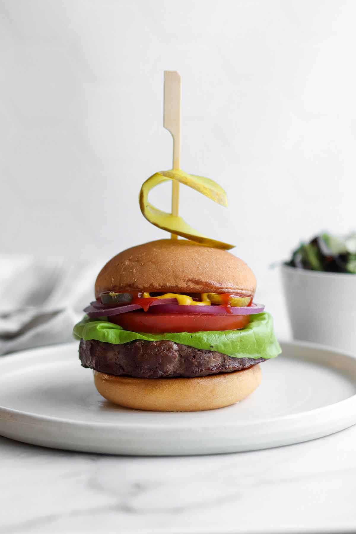 Elk burger sitting between a fluffy bun with all the fixings and placed on a modern white ceramic plate