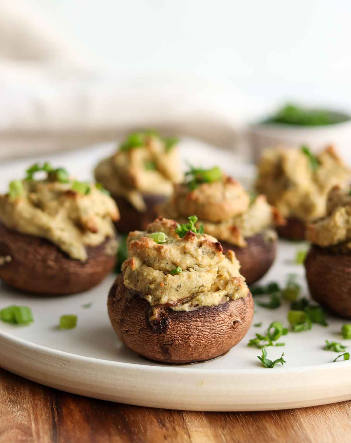 Close up view of stuffed mushroom caps on top of a modern white plate and sprinkled with chives