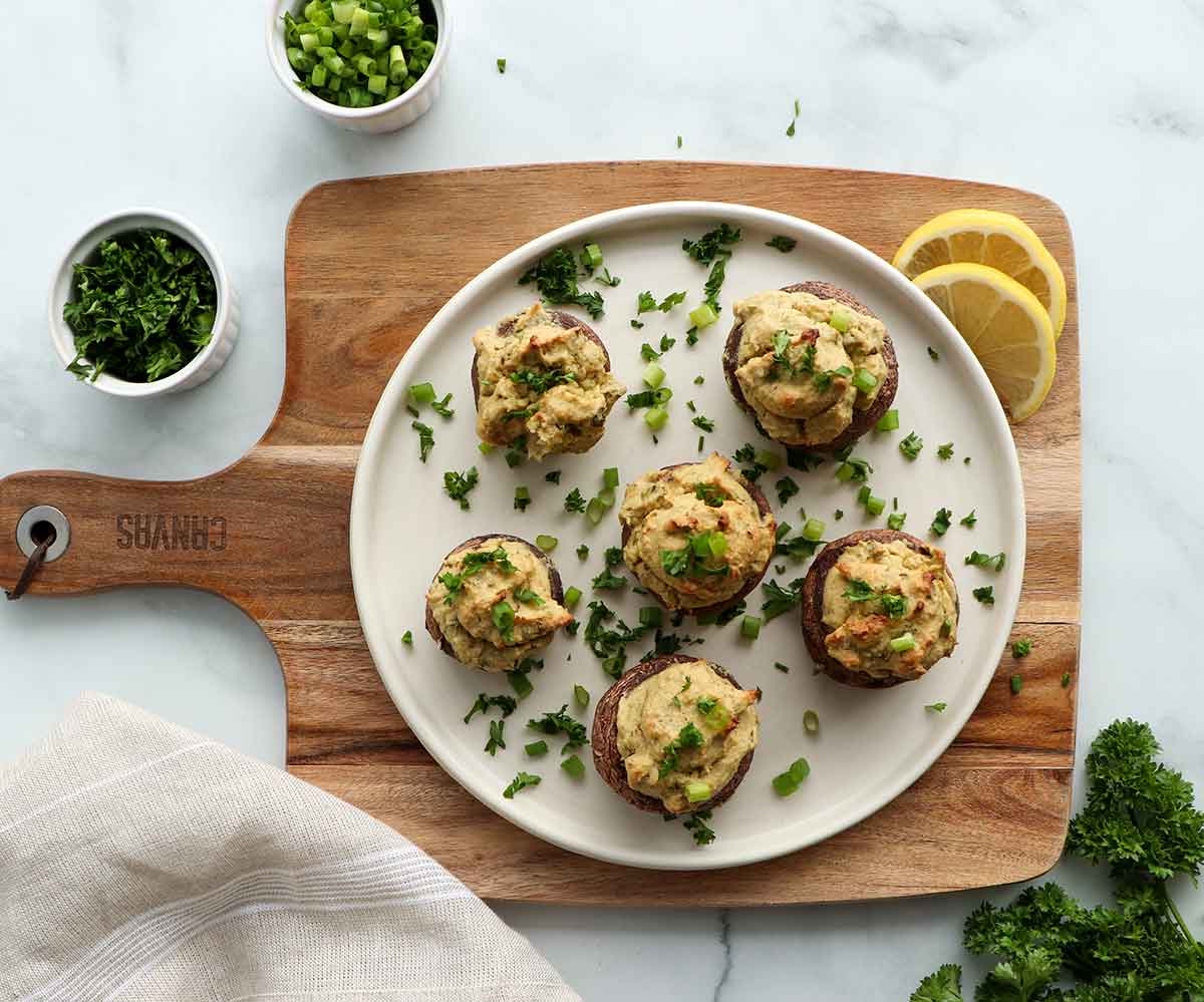 OVerhead view of stuffed mushroom caps placed on a wooden serving board surrounded by fresh and colourful ingredients