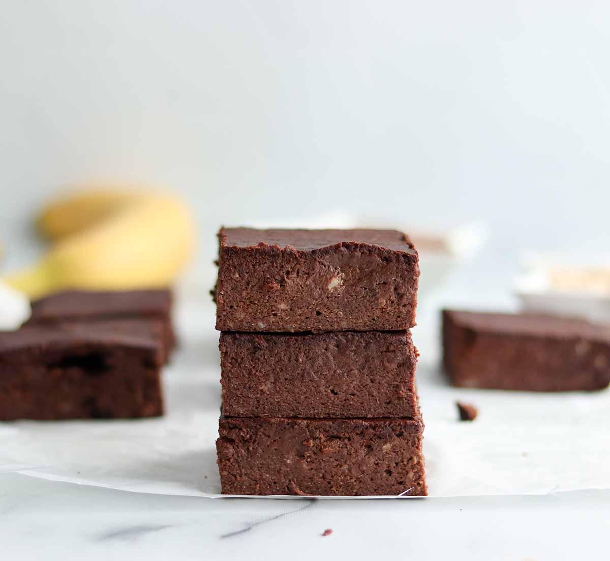 zoomed out view of stacked oat flour brownies with ingredients and more brownies in background