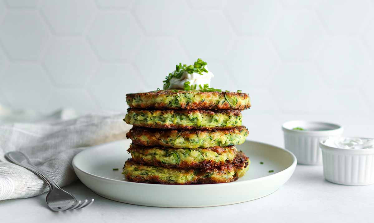 Side view of stacked zucchini fritters on a cream colored plate