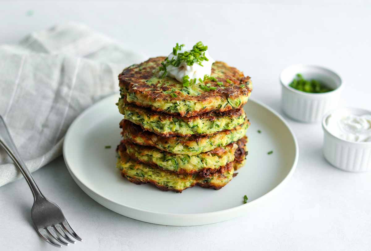 Zoomed out view of zucchini fritters stacked of a cream colored plate